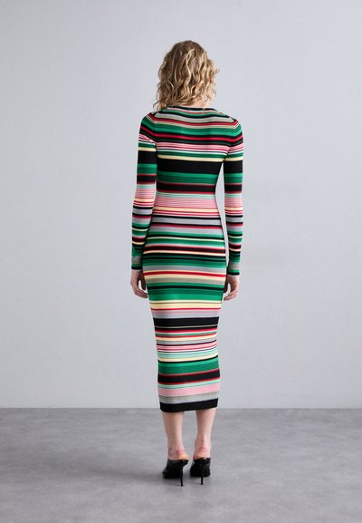 Abito a maniche lunghe a righe con linee orizzontali in verde, nero, rosa e rosso. Lunghezza a metà polpaccio con una silhouette aderente. Tacchi neri visibili.