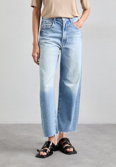 Lichtblauwe high-waisted jeans met een rechte pasvorm, voorzien van een vervaagde wassing en een rafelige zoom. Gecombineerd met zwarte sandalen met bandjes.