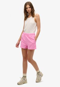 Roze katoenen shorts met een elastische tailleband en zijzakken, gecombineerd met een witte tanktop. Draag het met beige sneakers en gemusterde sokken.