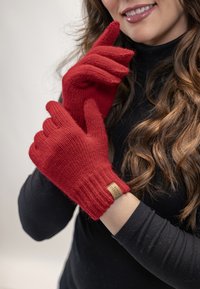 Røde strikkede handsker med ribbede manchetter, lavet af blødt materiale. Har et lille mærketag på håndleddet og en tætsiddende pasform på fingrene.