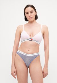 Svijetlopinkasti bralet s podesivim trakama, koji ima bijelu traku s natpisom "TOMMY HILFIGER". Uparen s donjim rubljem u tirkiznoj plavoj boji s uzorkom.
