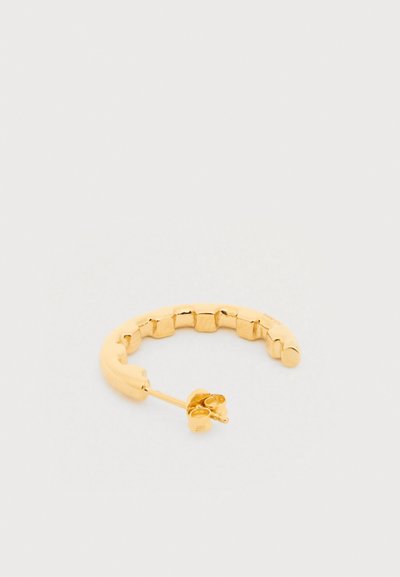 Zelta toņa pusapaļas auss gredzens ar sadalītu dizainu un tauriņa aizdari uz balta fona.