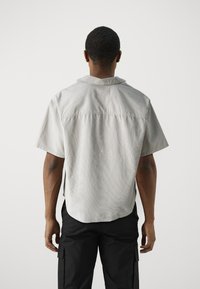 Kurzärmliges, hellgraues Hemd aus strukturiertem Stoff mit einem Camp-Kragen. Es hat eine Schulterpasse hinten und einen abgerundeten Saum.