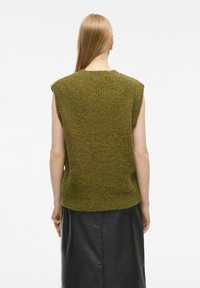 Bezrokavni zeleni pleteni pulover s teksturiranim zaključkom, ki ima širok ovratnik in rebrast rob, pari se z črno usnjeno krilom.