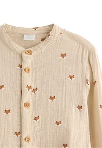 Beige Hemd mit Knöpfen und rundem Kragen, verziert mit kleinen gestickten Fuchs-Gesichtern. Hergestellt aus einem strukturierten, leichten Stoff mit Holzknöpfen.