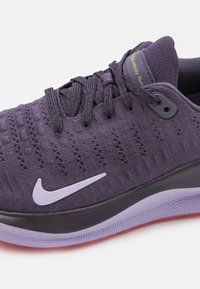 Nærbillede af en lilla Nike løbesko med strikket overdel, sort mellemsål og lilac og rød ydersål, snøret med mørkelilla snørebånd.