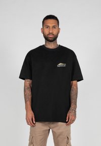 Sort bomulds t-shirt med korte ærmer, rund halsudskæring og et lille hvidt og gyldent logo på brystet. Enkel, afslappet pasform.