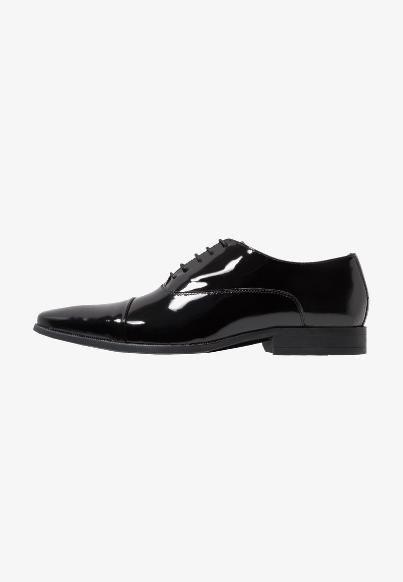 Zapato de vestir de charol negro con puntera afilada y seis ojetes. Presenta un acabado suave y un tacón bajo apilado.