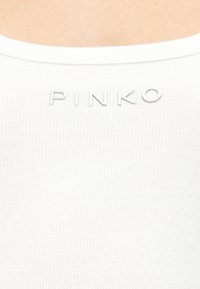 Κοντινό πλάνο λευκού ριμπ ύφανσης με ασημένια κεφαλαία γράμματα που σχηματίζουν τη λέξη "PINKO" κοντά στη γραμμή του λαιμού ενός αμάνικου τοπ.