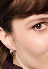 Srebrne kolczyki w kształcie kropli z polerowanym wykończeniem, uzupełnione małym akcentem przezroczystego kamienia szlachetnego.