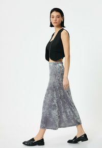 Sort cropped vest over en sort top, parret med en grå, lang, blødt struktureret nederdel. Sorte loafers fuldender outfittet.