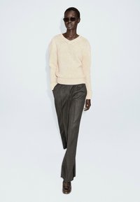 Pull en tricot rose clair avec un col en V et des poignets côtelés, associé à un pantalon tailleur gris foncé, doté de plis avant et de poches latérales.