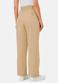 Beige wijde broek met een elastische tailleband, voorzien van een achterzak met een knoop. Gestyled met witte sneakers.