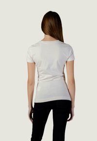 T-shirt ajusté à manches courtes en coton blanc, doté d'un col rond et d'une texture lisse. Porté avec un jean noir ajusté.