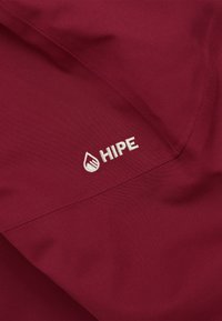 Bordeauxfarbener Stoff mit glatter Textur, versehen mit weißem, gesticktem "HIPE"-Logo und Wassertropfen-Design an der Seite.