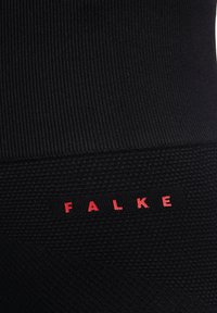 Zwarte textured stoffen legging met een geribbeld ontwerp en een geweven band met het woord "FALKE" in rode letters.