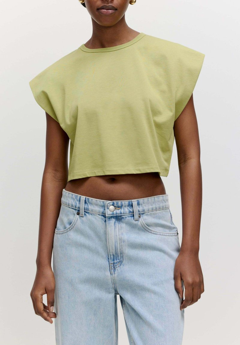 Kortaf olijfgroene t-shirt met brede, gestructureerde mouwen, gedragen met lichtblauwe high-waisted jeans met een knoopsluiting en zakken.