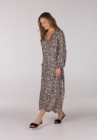 Lange, leopardprint jurk in beige en zwart met een V-halslijn en lange poffende mouwen, gecombineerd met zwarte instappers.