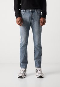 Lichtblauwe denim jeans met een rechte pasvorm, voorzien van een klassieke vijf-pocketontwerp en subtiele vervaging, gedragen met grijze en witte sneakers.