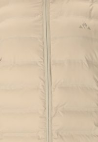 Puffjakke i lys beige med horisontale quiltede sektioner, der har en fuld lynlåslukning og minimal branding i det øverste højre hjørne.