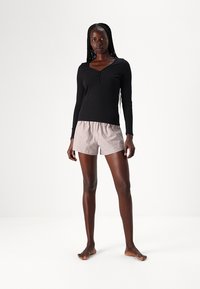 Schwarzes Langarmoberteil mit einem Henley-Ausschnitt, kombiniert mit hellrosa gestreiften Shorts. Die Shorts haben einen elastischen Bund und eine lockere Passform.