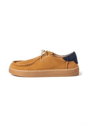 Chaussure décontractée en daim marron à lacets avec semelle en gomme et patch talon bleu foncé, vue de côté sur fond blanc.