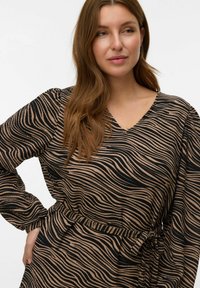 Robe à manches longues avec un col en V, présentant un motif ondulé noir et beige. Elle a une taille ceinturée et une texture côtelée.