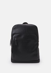 Sac à dos en cuir noir avec une texture lisse, un design mince, une poche zippée à l'avant et une poignée supérieure. Présente un logo discret à l'avant.