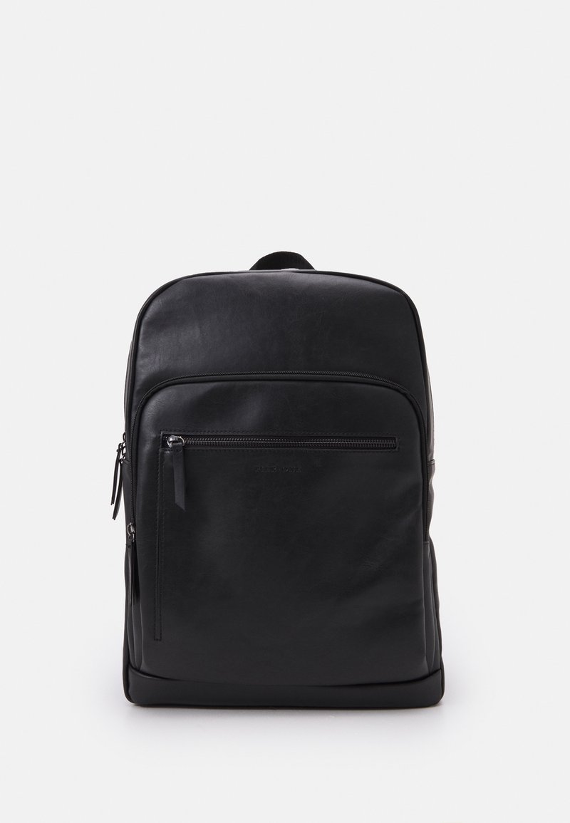Sac à dos en cuir noir avec une texture lisse, un design mince, une poche zippée à l'avant et une poignée supérieure. Présente un logo discret à l'avant.