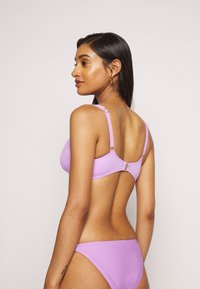 Conjunto de biquíni lilás com um top texturizado e alças ajustáveis, fechado com um gancho, combinado com partes de baixo de corte baixo de cor sólida.