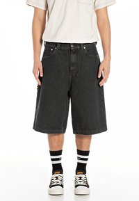 Black denim shorts with a loose fit, featuring large side pockets and a stitched hem. Worn with white sneakers and striped socks.