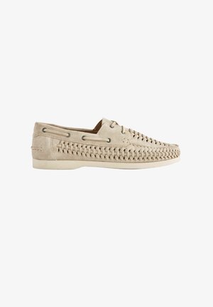 Beige suede loafer with woven detailing along sides and top, lace eyelets, and a flat rubber sole.