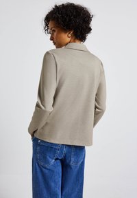 Top de manga larga beige con cuello, con una textura suave. Combinado con pantalones de mezclilla de pierna ancha azul, mostrando la vista trasera.