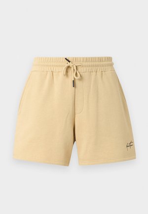 Short beige décontracté avec taille élastique et cordon, poches latérales, et petit logo signature noir sur la partie inférieure de la jambe droite.