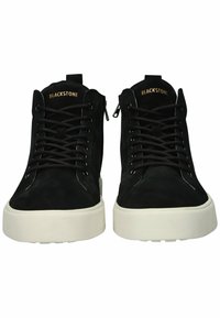 Zapatillas altas de ante negro con cordones negros y suelas de goma blanca. Presentan un logo en la lengua y una cremallera lateral para ponerlas y quitarlas fácilmente.