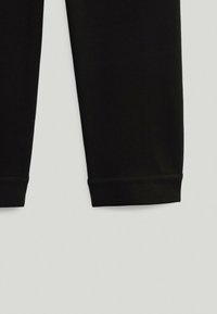 Jambes de pantalon en tissu noir avec des ourlets ajustés sur un fond gris clair, montrant la moitié inférieure du vêtement.