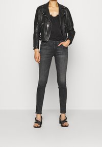 Chaqueta de moto de cuero negro con detalles acanalados en los hombros, top de tirantes con encaje negro, jeans ajustados grises y sandalias de tacón negro con tiras.