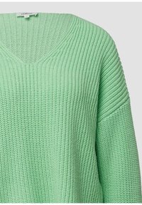 Hellgrüner Strickpullover mit V-Ausschnitt, Rippenstruktur und überschnittener Schulterpartie, der seinen weichen, atmungsaktiven Stoff betont.