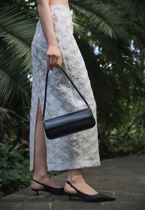 Osoba odjevena u bijelu teksturiranu midi suknju sa bočnim prorezom, crne slingback kitten pete, držeći crnu pravokutnu torbicu na otvorenom.