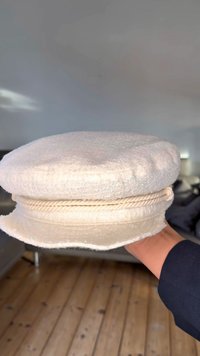 Valge tekstuuriga kangast müts ümarate krooniga ja punutud kaunistuspaelaga. Pehme, struktureeritud kuju; veidi laineline serv.