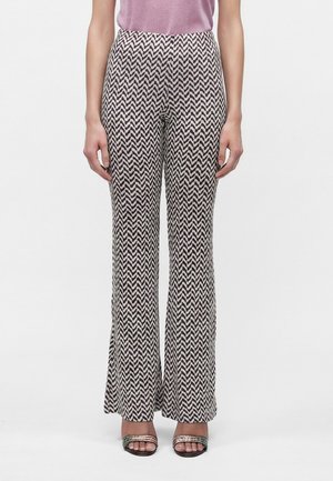 Femme portant un pantalon taille haute à jambes larges avec un motif zigzag noir et blanc et des sandales ouvertes à brides métalliques.