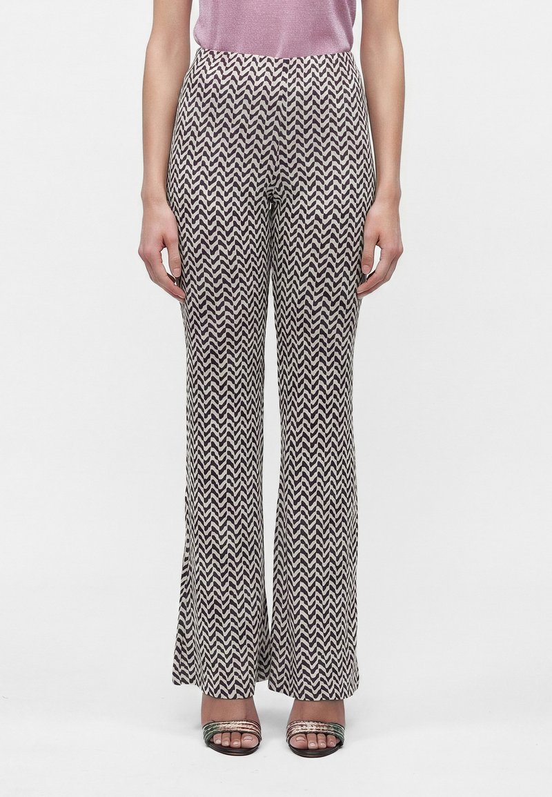 Femme portant un pantalon taille haute à jambes larges avec un motif zigzag noir et blanc et des sandales ouvertes à brides métalliques.