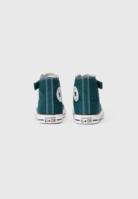 Tumedate rohelised kõrged Converse All Star kehavõisnepüksid kujutatud tagant, valgel taustal.