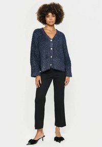 Navy blue fuzzy cardigan with a V-neck, five buttons, and wide sleeves, paired with black cropped trousers and black pointed toe shoes.
