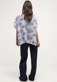 Blusa ligera con estampado floral en blanco y azul, de mangas cortas, corte holgado, combinada con pantalones oscuros de color azul marino. Textura suave, diseño casual.