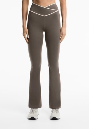 Leggings maro cu flared și un design asimetric al taliei, având un accent de culoare deschisă de-a lungul taliei și pe cusăturile laterale.