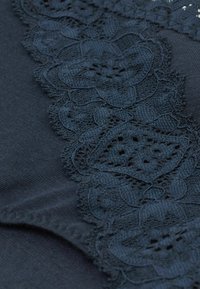 Zwarte stof met complexe kantdetails met bloemmotieven en uitsnedelementen langs één rand, wat textuur en contrast toevoegt.