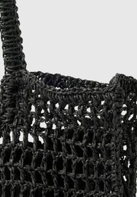 Schwarze gewebte Tragetasche aus strukturiertem Material. Verfügt über ein offenes Mesh-Design und stabile, geflochtene Griffe.