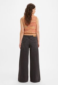 Värgglad ärmlös stickad topp med en texturerad mönster, kombinerad med högmidjade vida svarta denimbyxor med bakfickor.