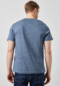 Modrý pruhovaný trikotaž s měkké tkaniny, který má bílé vodorovné pruhy, kulatý výstřih a krátké rukávy. Nosí se s tmavými džíny.